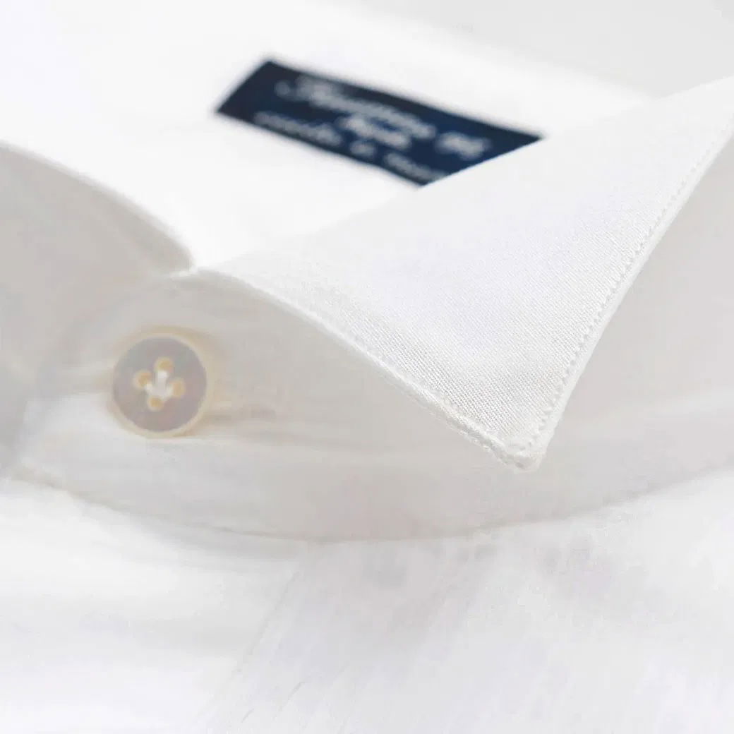 Weißes Herrenhemd mit spitzem Kragen, sichtbarem Knopf und dunkelblauem Etikett im Kragenbereich. Weißes Herrenhemd mit spitzem Kragen, sichtbarem Knopf und dunkelblauem Etikett im Kragenbereich.