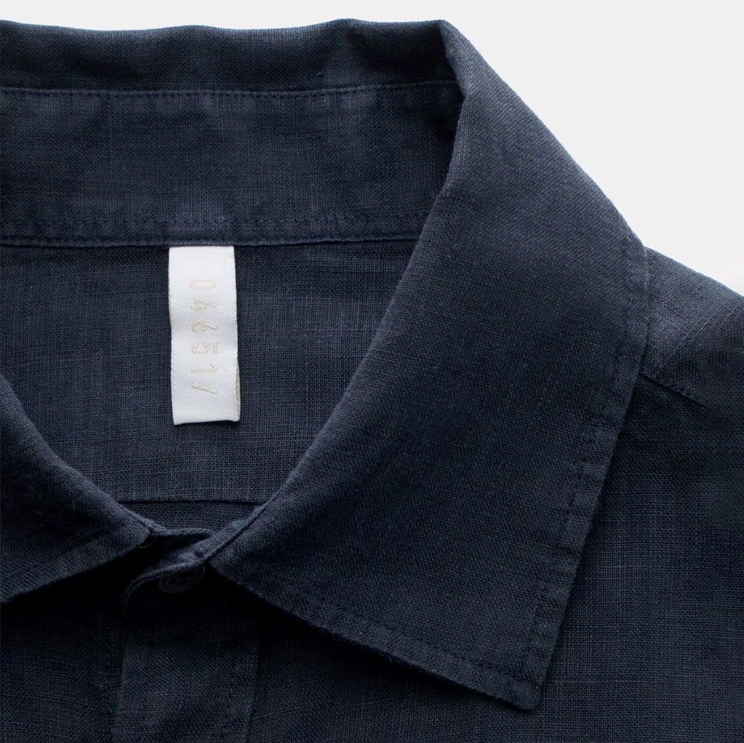 Dunkelblaues Kurzarmhemd aus Leinen mit Kragen und weißem Größenlabel '04651' an der Innenseite. Dunkelblaues Kurzarmhemd aus Leinen mit Kragen und weißem Größenlabel '04651' an der Innenseite.