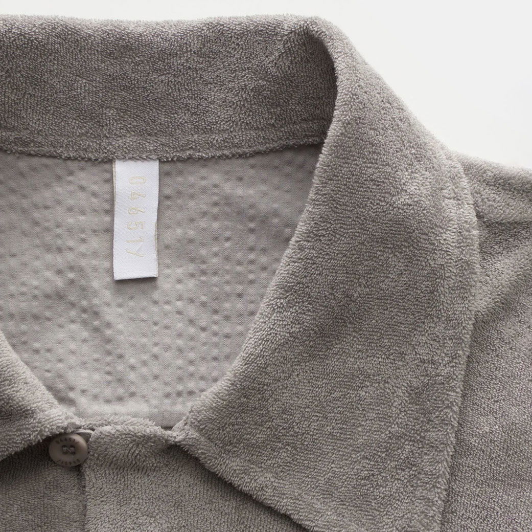 Graues Frottee-Kurzarmhemd mit offenem Kragen, sichtbarem weißen Designerlabel und feiner Struktur im Stoff. Graues Frottee-Kurzarmhemd mit offenem Kragen, sichtbarem weißen Designerlabel und feiner Struktur im Stoff.