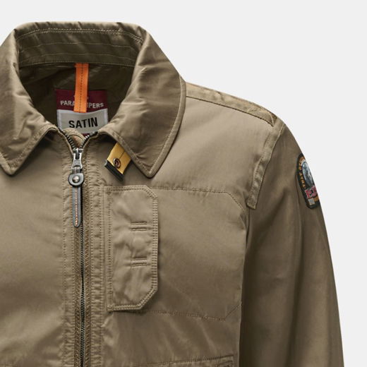 Detailansicht einer olivgrünen Herrenjacke mit Reißverschluss, Stehkragen, Brusttasche und aufgenähtem Ärmel-Patch.