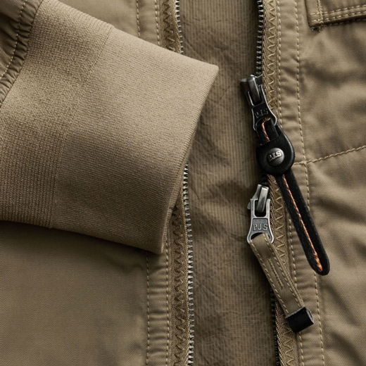 Detailaufnahme eines olivgrünen Herrenjacken-Ärmels mit geripptem Bündchen und zwei Reißverschlüssen mit PJS-Zippern.