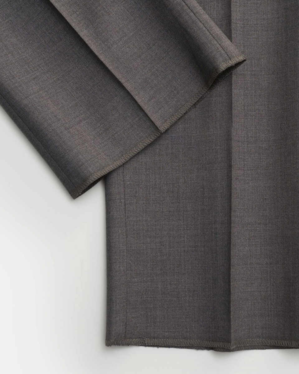 Detailaufnahme des Saums einer grauen Herrenhose mit Bundfalte, feiner Stoffstruktur und sauberer Verarbeitung.