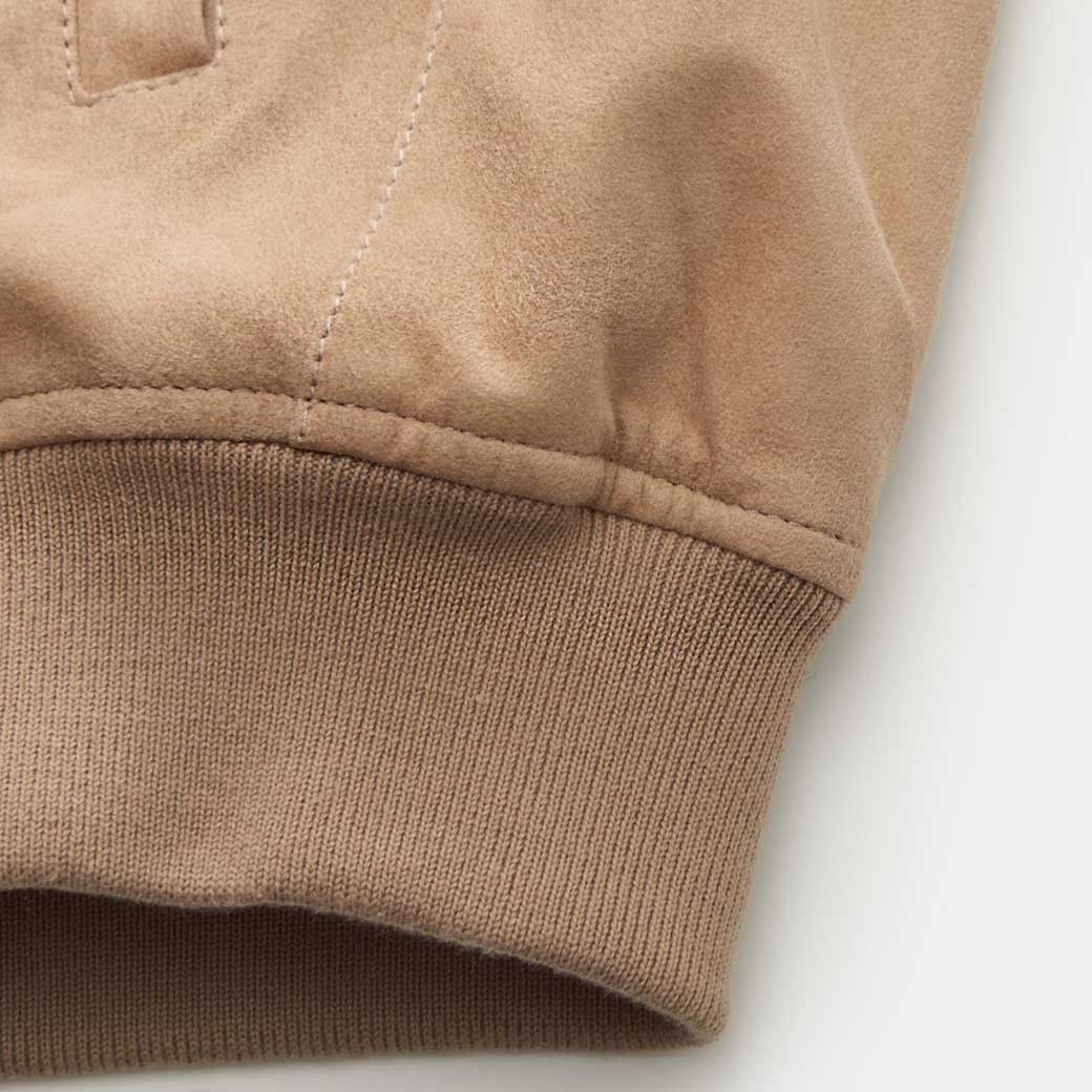 Detailaufnahme des beigen Velourslederblouson-Saums mit elastischem, geripptem Strickbund für Herren.