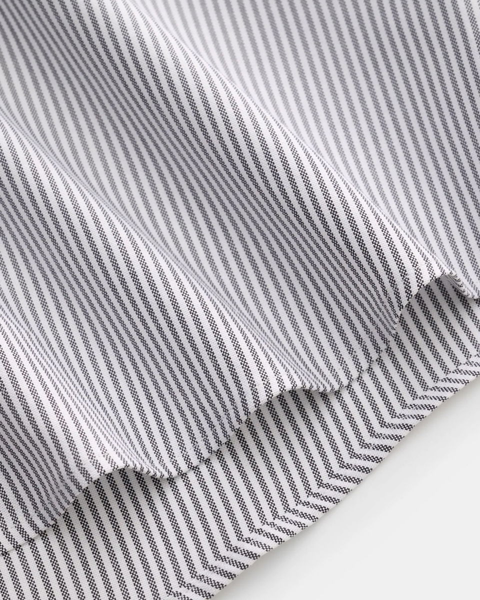 Detailaufnahme des Saums eines weiß-grau gestreiften Herrenhemdes mit feinen, senkrechten Linien.