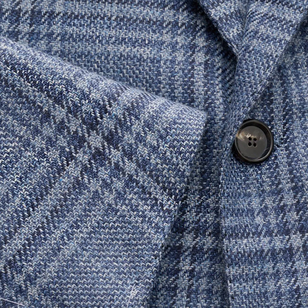 Hellblau-dunkelblau kariertes Wollstoff-Detail eines Sakkos mit sichtbarem schwarzem Knopf und feiner Struktur.