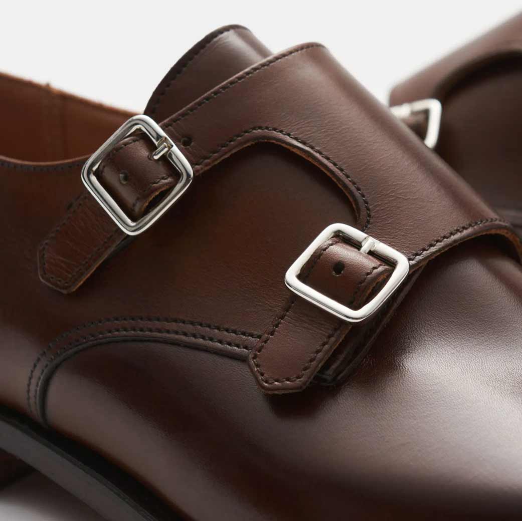 Dunkelbraune Lederschuhe mit Doppelmonk-Verschluss und silbernen Schnallen, feine Nahtdetails sichtbar.