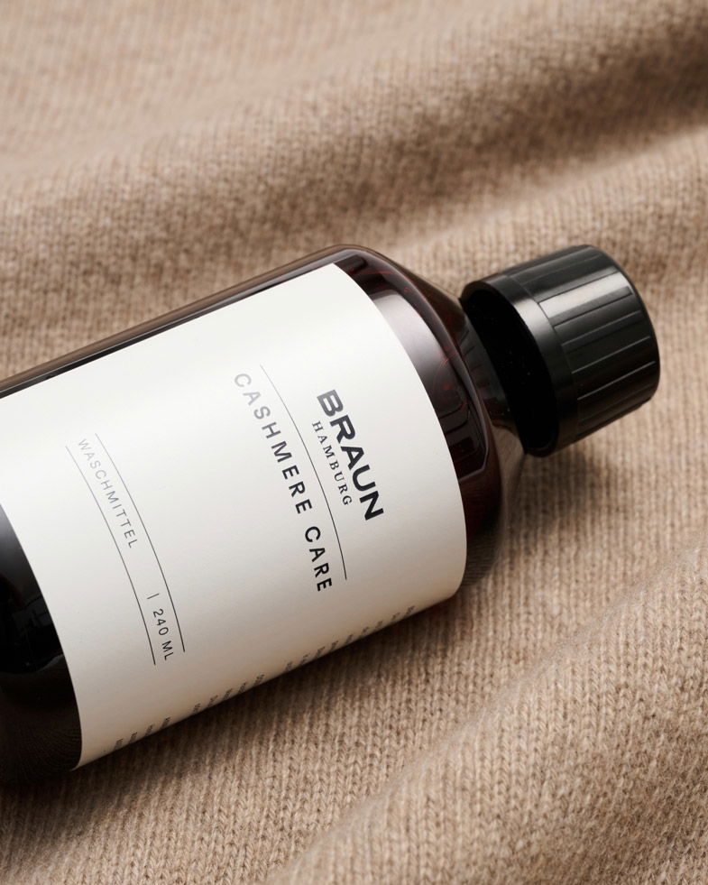 Flasche BRAUN Hamburg Cashmere Care Waschmittel 240 ml auf beige Strickstoff liegend, Nahaufnahme. Flasche BRAUN Hamburg Cashmere Care Waschmittel 240 ml auf beige Strickstoff liegend, Nahaufnahme.