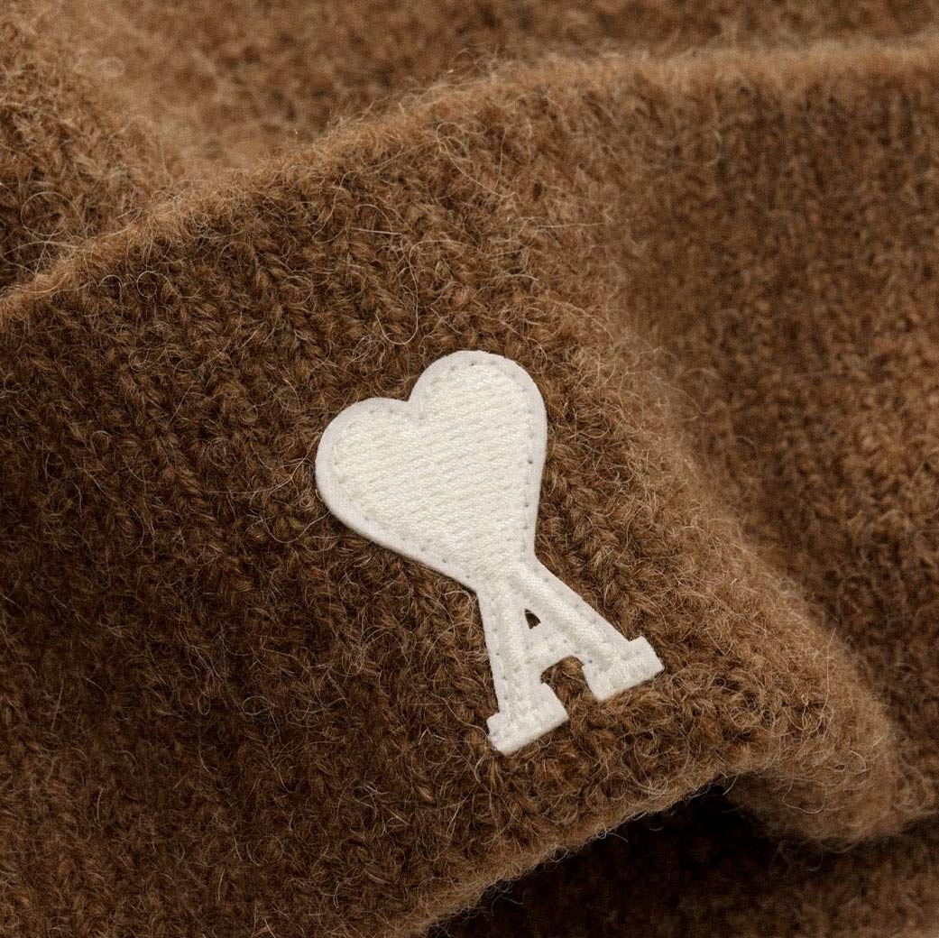 Detailaufnahme einer braunen Kaschmirmütze mit weißem Ami Paris Designerlogo in Herzform. Detailaufnahme einer braunen Kaschmirmütze mit weißem Ami Paris Designerlogo in Herzform.