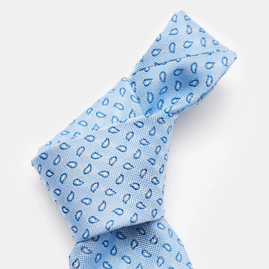 Hellblaue Krawatte mit feinem, dunkelblauem Paisley-Muster, elegant gebunden vor hellem Hintergrund.