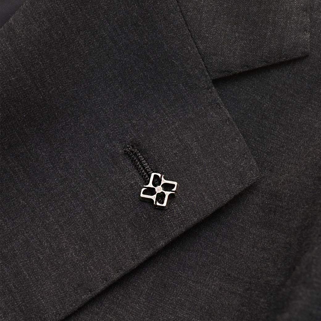 Silberne Brosche in Kreuzform am Revers eines schwarzen Herren-Sakkos, Nahaufnahme mit feiner Stoffstruktur.