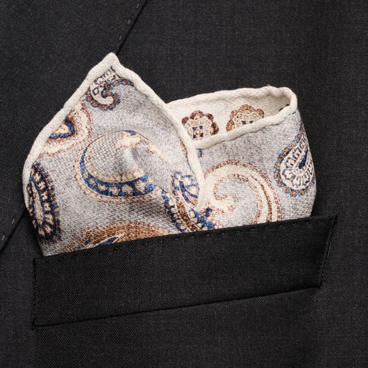 Detailaufnahme eines weißen Einstecktuchs mit blau-braunem Paisley-Muster in der Brusttasche eines schwarzen Sakkos. Detailaufnahme eines weißen Einstecktuchs mit blau-braunem Paisley-Muster in der Brusttasche eines schwarzen Sakkos.