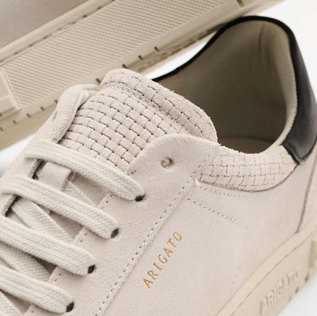 Hellgrauer Herren-Sneaker aus Veloursleder mit geflochtener Zunge, weißen Schnürsenkeln und goldfarbener Designeraufschrift 'ARIGATO'.