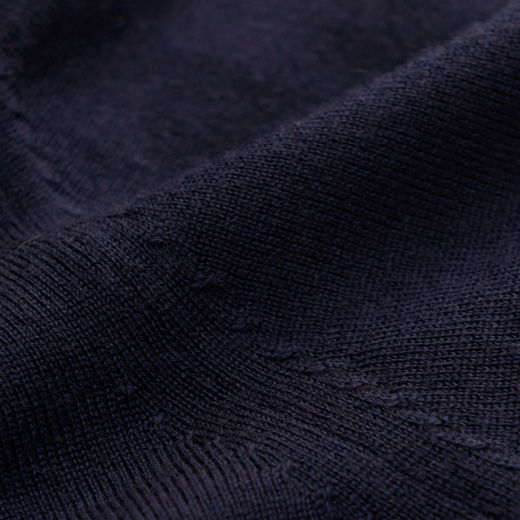 Detaillierte Nahaufnahme eines dunkelblauen Merinopullovers mit feiner, weicher Strickstruktur und sichtbarer Naht. Detaillierte Nahaufnahme eines dunkelblauen Merinopullovers mit feiner, weicher Strickstruktur und sichtbarer Naht.
