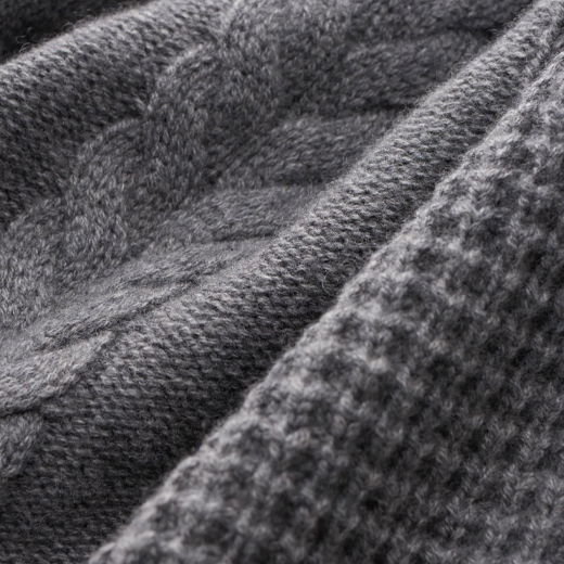 Grau melierter Strickstoff mit detailreichem Zopfmuster und fein strukturierter, weicher Oberfläche, Nahaufnahme. Grau melierter Strickstoff mit detailreichem Zopfmuster und fein strukturierter, weicher Oberfläche, Nahaufnahme.
