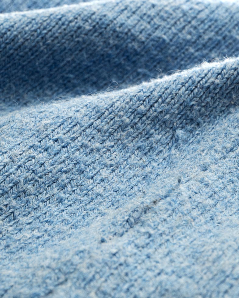 Nahaufnahme eines blauen Wollstoffes mit sichtbarem Pilling und feiner, strukturierter Strickmaschen-Oberfläche. Nahaufnahme eines blauen Wollstoffes mit sichtbarem Pilling und feiner, strukturierter Strickmaschen-Oberfläche.