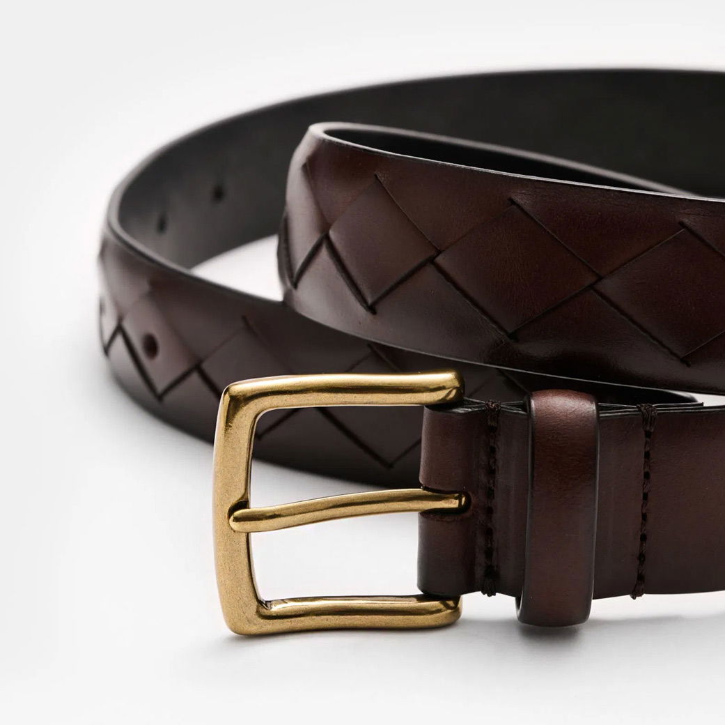 Brauner Ledergürtel mit geflochtenem Muster und goldener Metall-Gürtelschnalle, auf weißem Hintergrund.