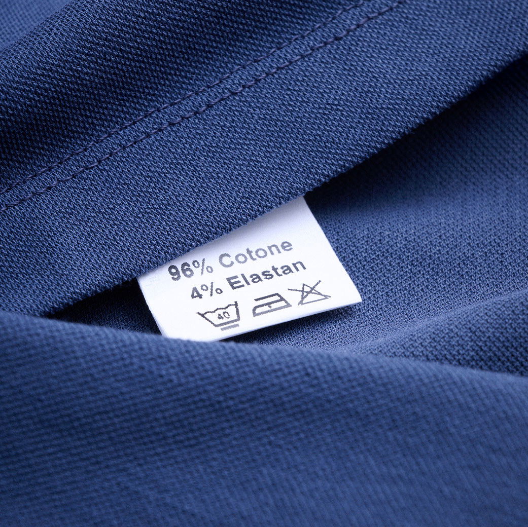 Detailaufnahme eines dunkelblauen Jersey-Stoffs mit einem weißen Pflegeetikett, das Material- und Waschanweisungen zeigt.