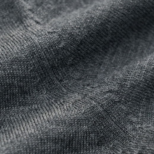 Detaillierte Nahaufnahme eines dunkelgrauen, fein gestrickten Pullovers aus weicher Merinowolle mit sichtbarer Textur.