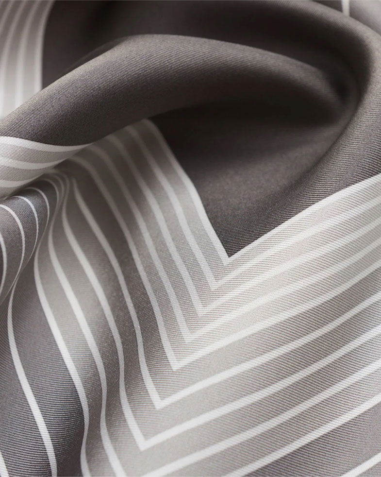 Grau-weiß gemustertes Einstecktuch aus Seide mit feinen, parallelen Linien und weichen Falten in Nahaufnahme.