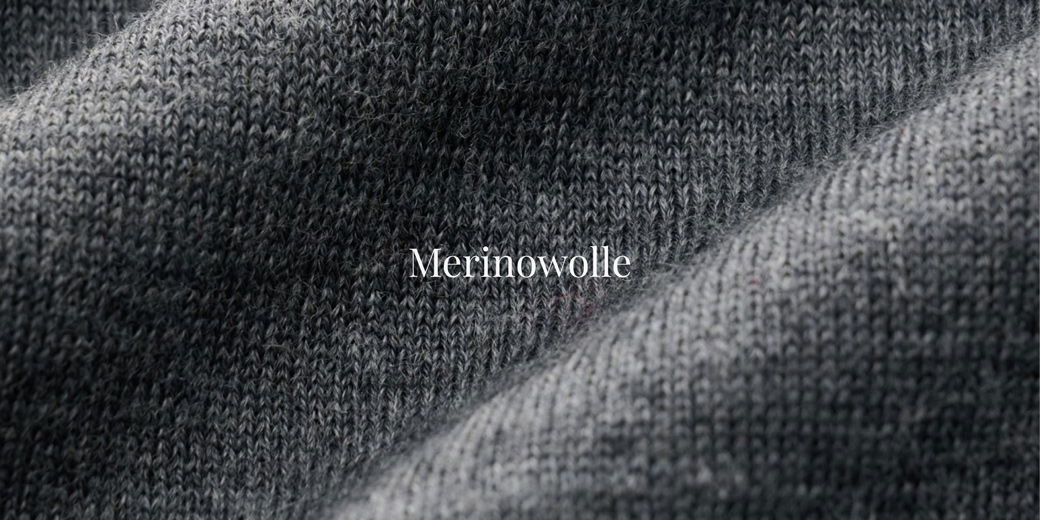 Detailaufnahme eines grauen Merinowoll-Pullovers mit sichtbarer Strickstruktur und weißem Schriftzug „Merinowolle“.