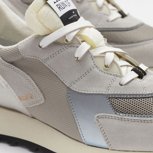 Hellgrauer Herren-Sneaker aus Wildleder und Mesh mit weißen Schnürsenkeln und hellblauen Details, Nahaufnahme. Hellgrauer Herren-Sneaker aus Wildleder und Mesh mit weißen Schnürsenkeln und hellblauen Details, Nahaufnahme.