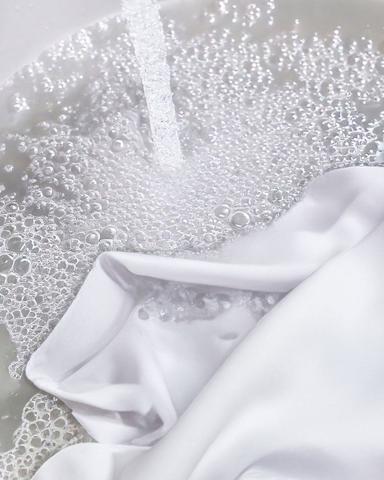 Weißes Shirt wird in Wasser eingeweicht, umgeben von sprudelnden Luftblasen und Wasserstrahl, Nahaufnahme.