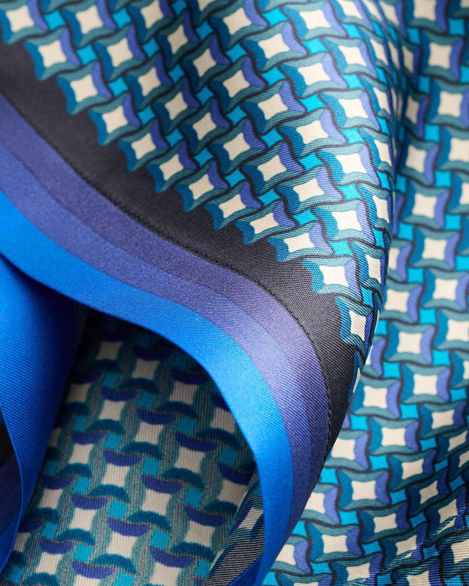 Detailansicht eines Seidenstoffs mit blau-lila-weißem geometrischem Muster und farbigem Streifenrand. Detailansicht eines Seidenstoffs mit blau-lila-weißem geometrischem Muster und farbigem Streifenrand.