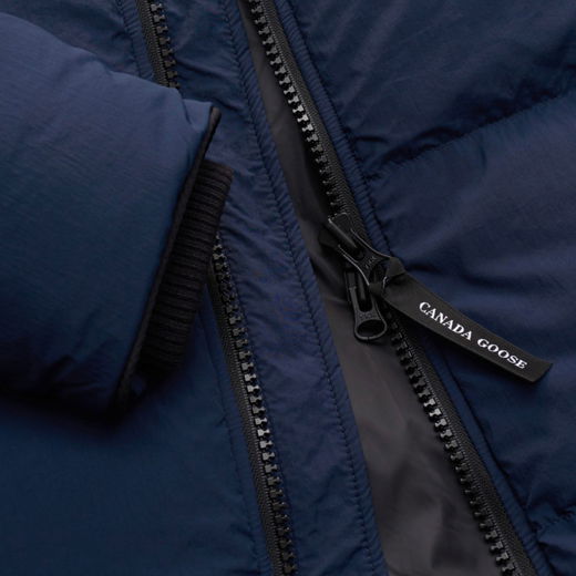 Detailaufnahme eines dunkelblauen Canada Goose Daunenjacken-Reißverschlusses mit schwarzem Designerprint-Zipper und Ärmelbündchen. Detailaufnahme eines dunkelblauen Canada Goose Daunenjacken-Reißverschlusses mit schwarzem Designerprint-Zipper und Ärmelbündchen.
