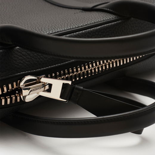 Schwarze Leder-Aktentasche mit silbernem Metall-Reißverschluss und zwei schwarzen Leder-Tragegriffen im Detail. Schwarze Leder-Aktentasche mit silbernem Metall-Reißverschluss und zwei schwarzen Leder-Tragegriffen im Detail.