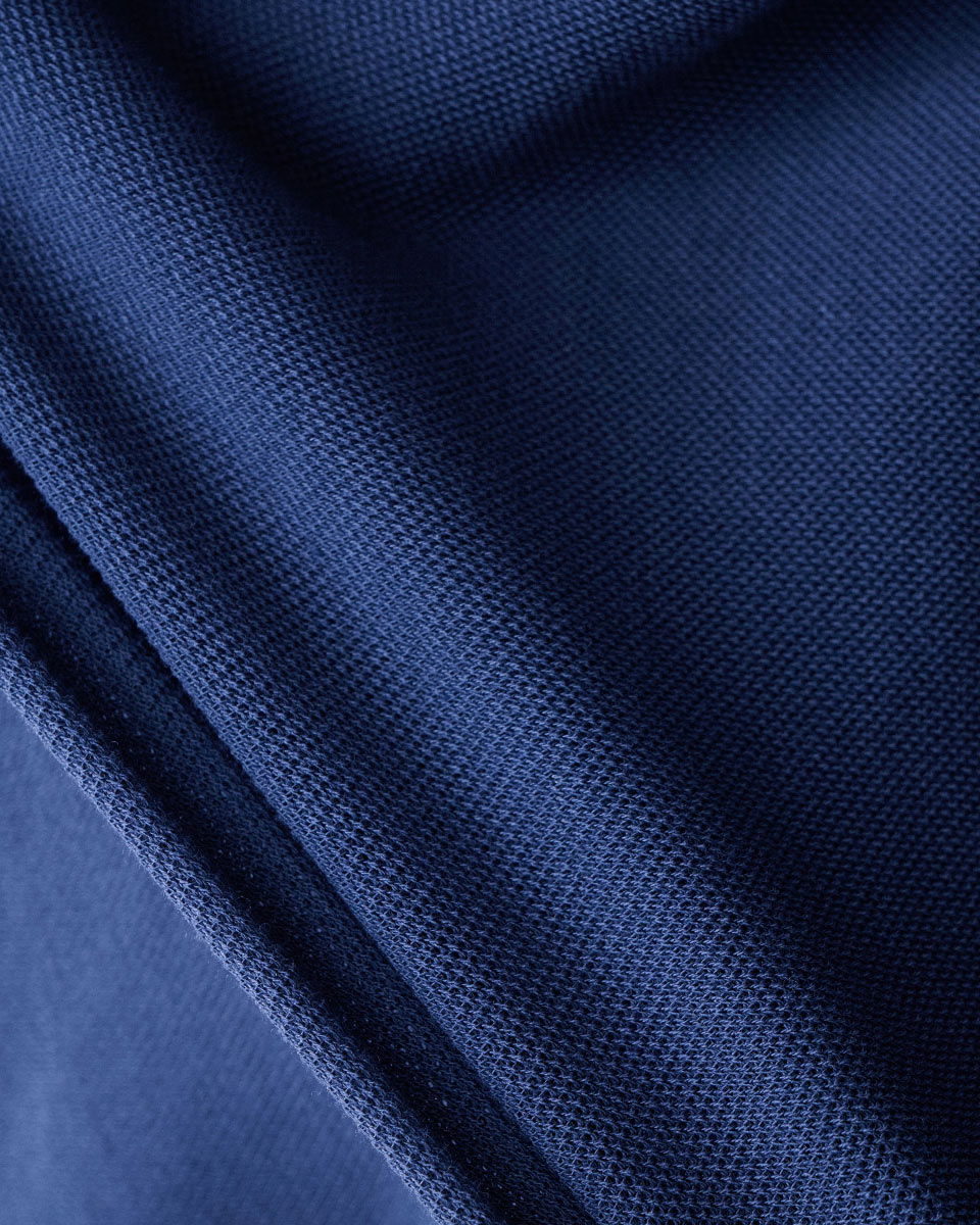 Dunkelblauer Jersey-Stoff mit feiner Struktur in Falten gelegt, Nahaufnahme der textile Oberfläche und Maschen.
