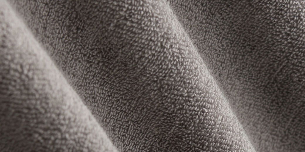 Detailaufnahme eines dunkelgrauen Frotteestoffes mit weicher, strukturierter Oberfläche und feinen Schlingen. Detailaufnahme eines dunkelgrauen Frotteestoffes mit weicher, strukturierter Oberfläche und feinen Schlingen.