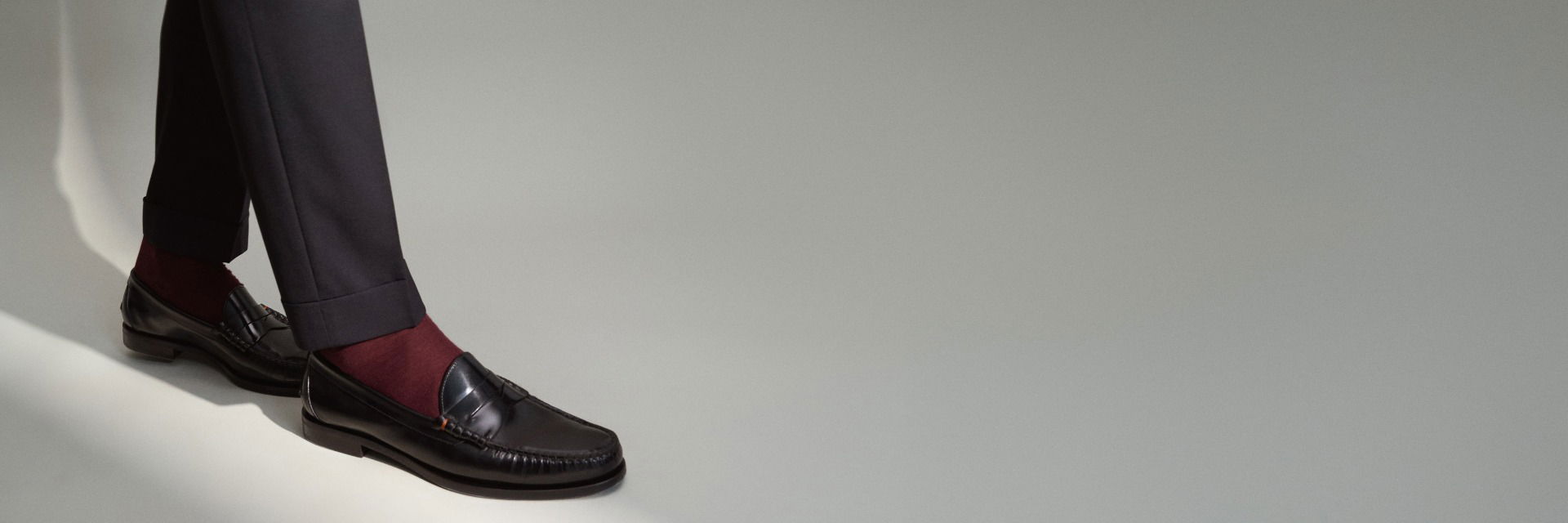 Detailaufnahme von schwarzen Loafern mit roten Socken und schwarzer Hose auf hellgrauem Hintergrund, getragen von einer Person. Detailaufnahme von schwarzen Loafern mit roten Socken und schwarzer Hose auf hellgrauem Hintergrund, getragen von einer Person.