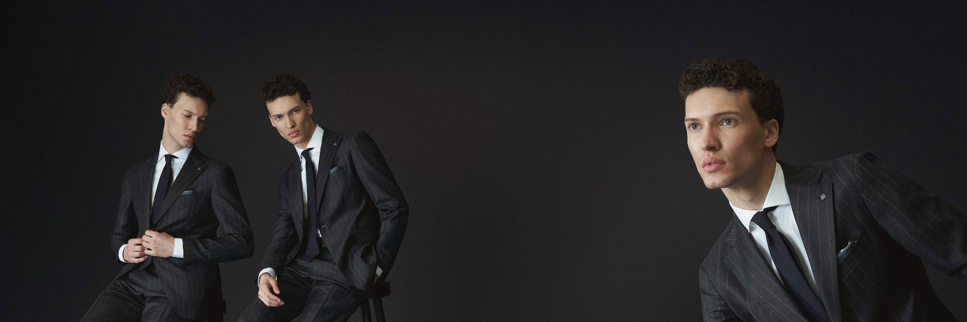 Drei junge Männer in dunkelgrauen Nadelstreifenanzügen mit weißen Hemden und dunkelblauen Krawatten vor schwarzem Hintergrund. Drei junge Männer in dunkelgrauen Nadelstreifenanzügen mit weißen Hemden und dunkelblauen Krawatten vor schwarzem Hintergrund.