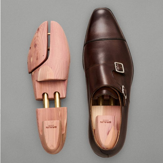 Brauner Herrenschuh aus Leder mit Doppelschnalle, daneben ein natürlicher Holz-Schuhspanner aus Zedernholz, Vogelperspektive.