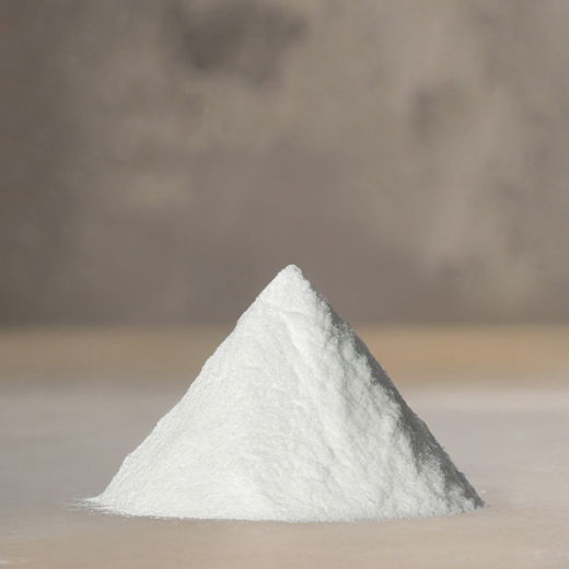 Ein kleiner, weißer, fein gemahlener Haufen Backpulver auf einer glatten, hellen Oberfläche vor unscharfem Hintergrund.