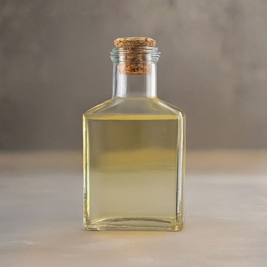 Glasflasche mit hellem Essig, quadratisch, mit Korkverschluss, vor unscharfem beigem Hintergrund stehend.