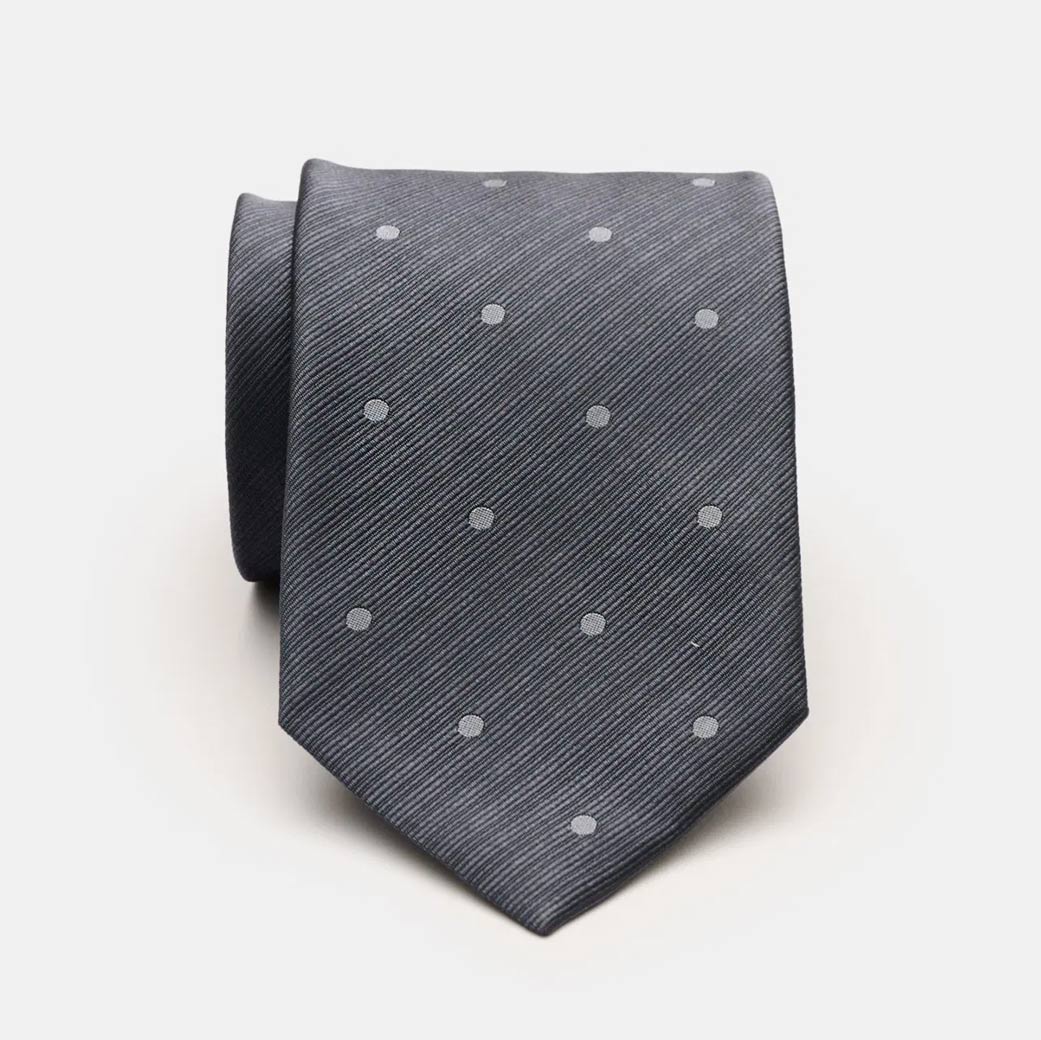 Dunkelgraue, eingerollte Krawatte mit diagonalen Linien und hellgrauen, gleichmäßig verteilten Punkten auf hellem Hintergrund.