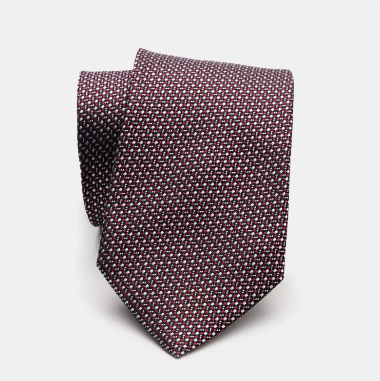 Eingerollte Seidenkrawatte in Dunkelrot mit feinem Muster aus kleinen weißen und hellblauen Punkten vor weißem Hintergrund.