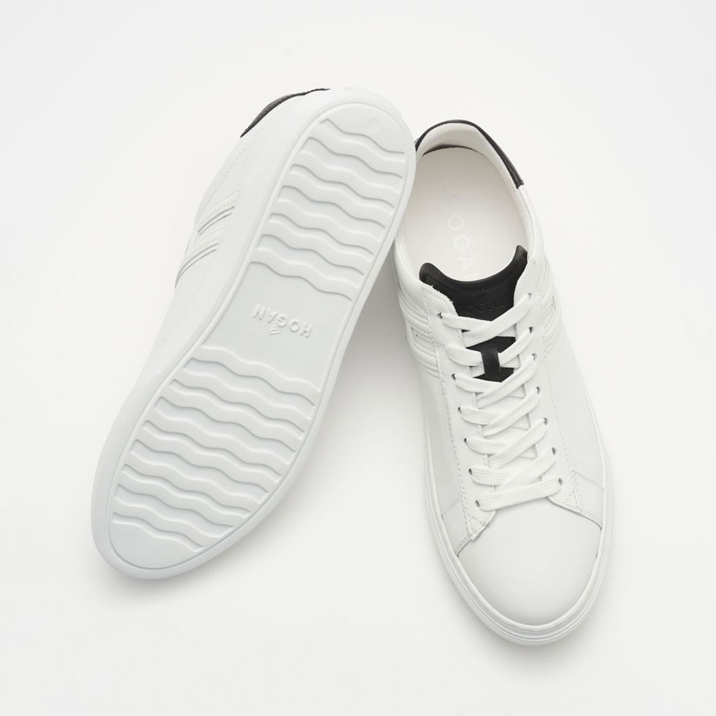 Weiße Herrensneaker aus Leder mit schwarzer Lasche, weißer Sohle und weißen Schnürsenkeln, freistehend auf weißem Hintergrund. Weiße Herrensneaker aus Leder mit schwarzer Lasche, weißer Sohle und weißen Schnürsenkeln, freistehend auf weißem Hintergrund.