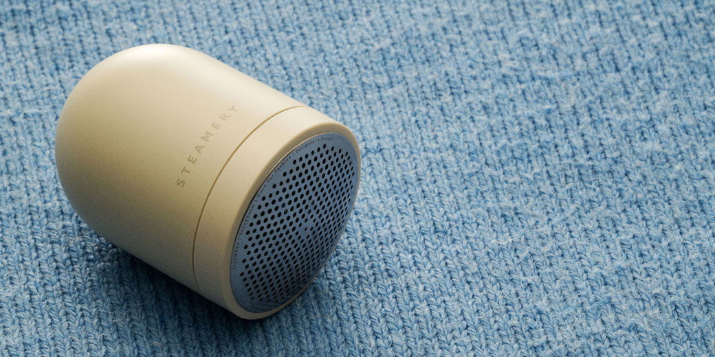 Beiger Fusselrasierer liegt auf einem hellblauen, grob gestrickten Pullover aus Wolle, Nahaufnahme. Beiger Fusselrasierer liegt auf einem hellblauen, grob gestrickten Pullover aus Wolle, Nahaufnahme.