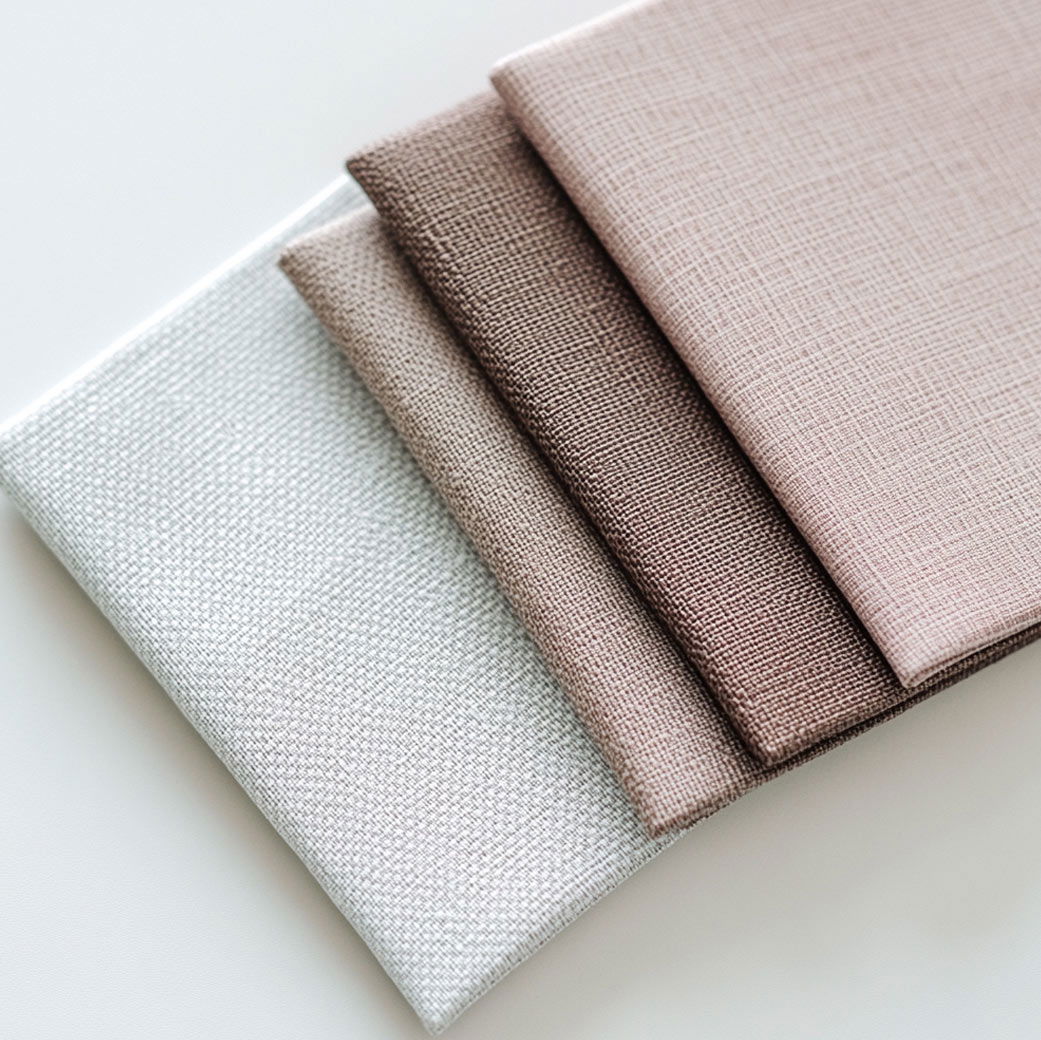 Gefaltete Stoffstücke in den Farben Weiß, Beige, Taupe und Braun mit feiner, gewebter Struktur auf hellem Untergrund.