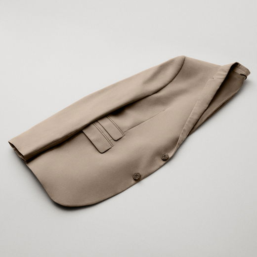 Beige Herren-Sakko liegt gefaltet und gelegt auf hellgrauem Untergrund, mit sichtbaren Knöpfen und Taschenklappen.