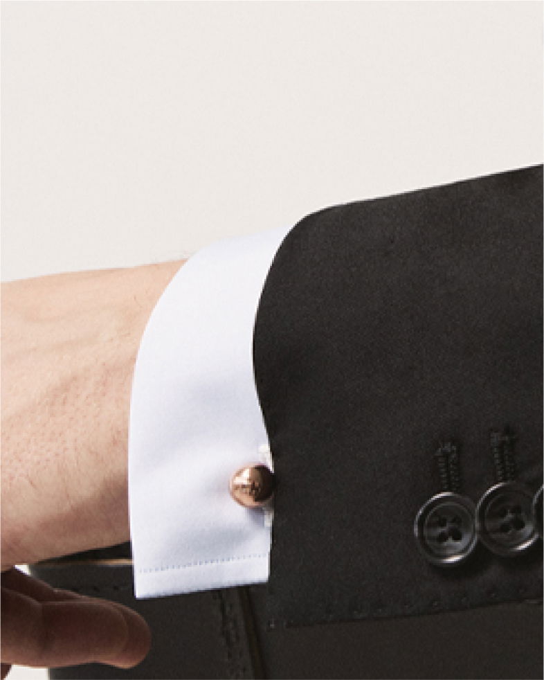 Weißes Hemd mit goldfarbenem Manschettenknopf, getragen unter einem schwarzen Sakko mit schwarzen Knöpfen. Weißes Hemd mit goldfarbenem Manschettenknopf, getragen unter einem schwarzen Sakko mit schwarzen Knöpfen.