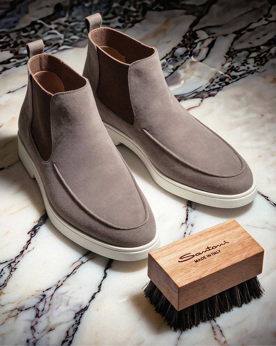 Hellgraue Herren-Boots aus Wildleder auf Marmor mit brauner Schuhbürste aus Holz und schwarzen Borsten. Hellgraue Herren-Boots aus Wildleder auf Marmor mit brauner Schuhbürste aus Holz und schwarzen Borsten.
