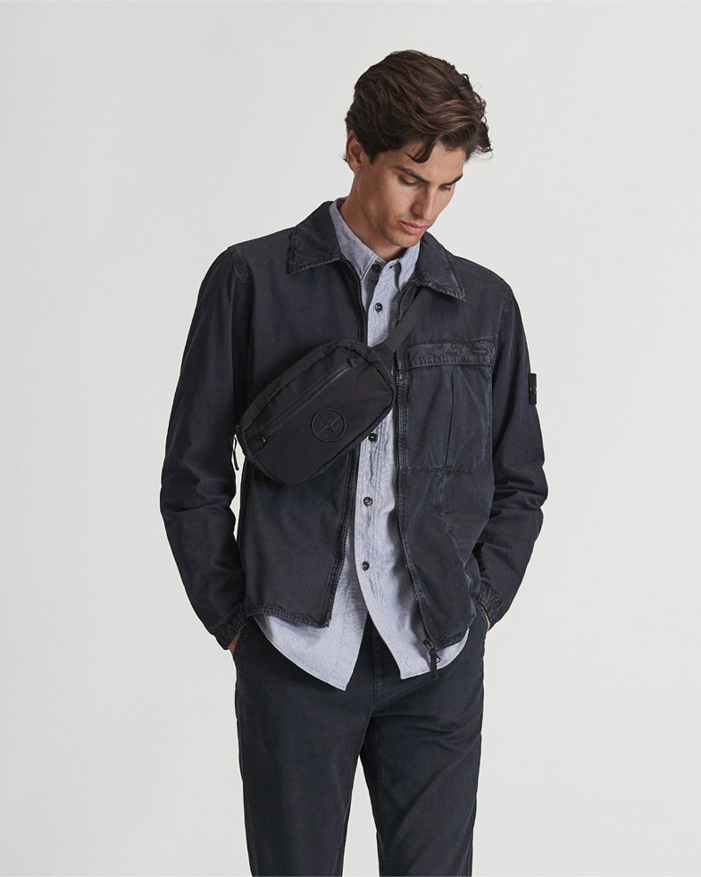 Mann trägt dunkelblaue Jacke, hellblaues Hemd, schwarze Hose und schwarze Gürteltasche quer vor der Brust, schaut nach unten. Mann trägt dunkelblaue Jacke, hellblaues Hemd, schwarze Hose und schwarze Gürteltasche quer vor der Brust, schaut nach unten.