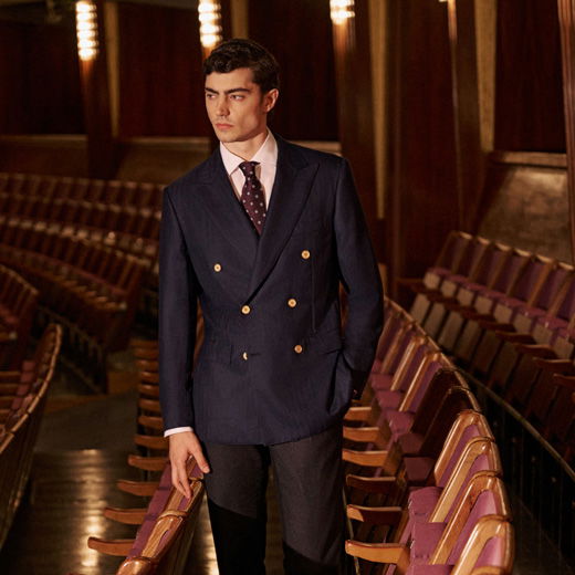 Mann in blauem Sakko, weißem Hemd und gemusterter Krawatte steht in einem alten Theater zwischen roten Sitzreihen, Blick seitlich. Mann in blauem Sakko, weißem Hemd und gemusterter Krawatte steht in einem alten Theater zwischen roten Sitzreihen, Blick seitlich.