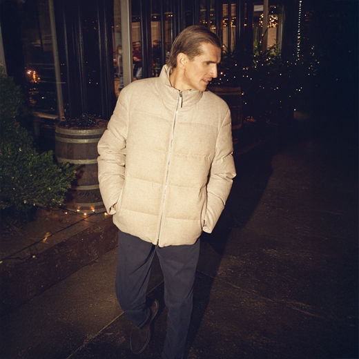 Mann in beiger Daunenjacke und blauer Hose läuft nachts an weihnachtlich beleuchtetem Außenbereich mit Tannenbäumen vorbei. Mann in beiger Daunenjacke und blauer Hose läuft nachts an weihnachtlich beleuchtetem Außenbereich mit Tannenbäumen vorbei.