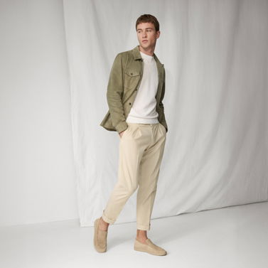 Mann trägt beige Chinohose, weißes Shirt, olivgrünes Overshirt und beige Loafer, steht vor hellem Hintergrund. Mann trägt beige Chinohose, weißes Shirt, olivgrünes Overshirt und beige Loafer, steht vor hellem Hintergrund.