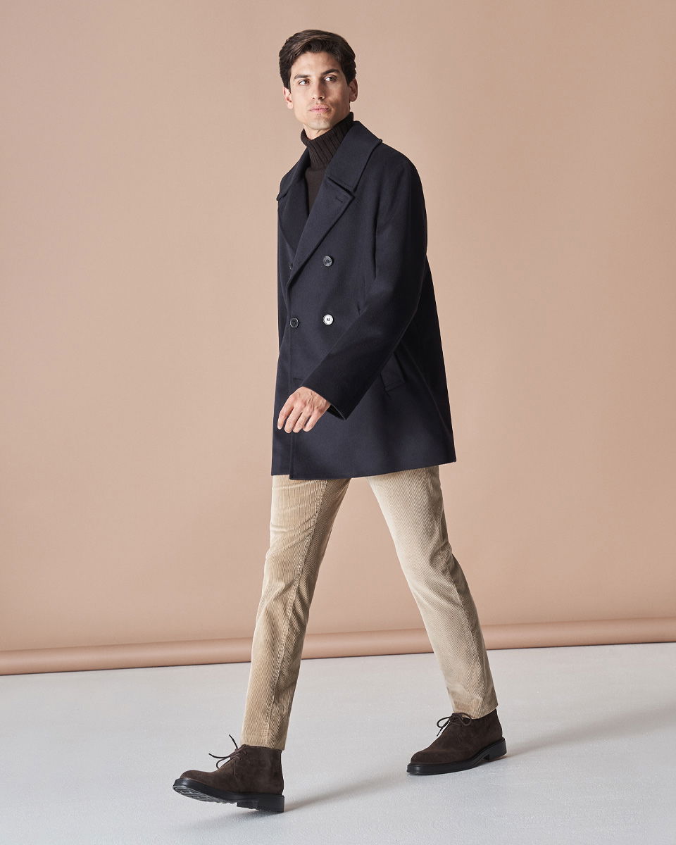 Mann trägt dunkelblauen Mantel, braunen Rollkragenpullover, beige Cordhose und dunkelbraune Schnürstiefel, geht nach links. Mann trägt dunkelblauen Mantel, braunen Rollkragenpullover, beige Cordhose und dunkelbraune Schnürstiefel, geht nach links.