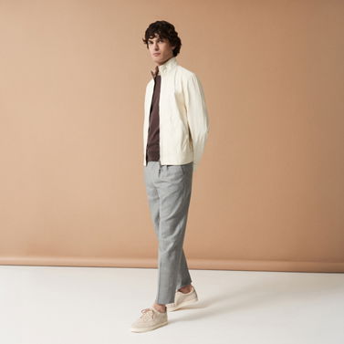 Mann mit hellgrauer Hose, braunem Shirt, cremefarbener Jacke und beigen Sneakern vor beige-braunem Hintergrund. Mann mit hellgrauer Hose, braunem Shirt, cremefarbener Jacke und beigen Sneakern vor beige-braunem Hintergrund.